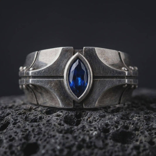 A sterling silver ring with an oxidized finish and marquise blue stone displayed on textured volcanic rock in a premium macro shot.