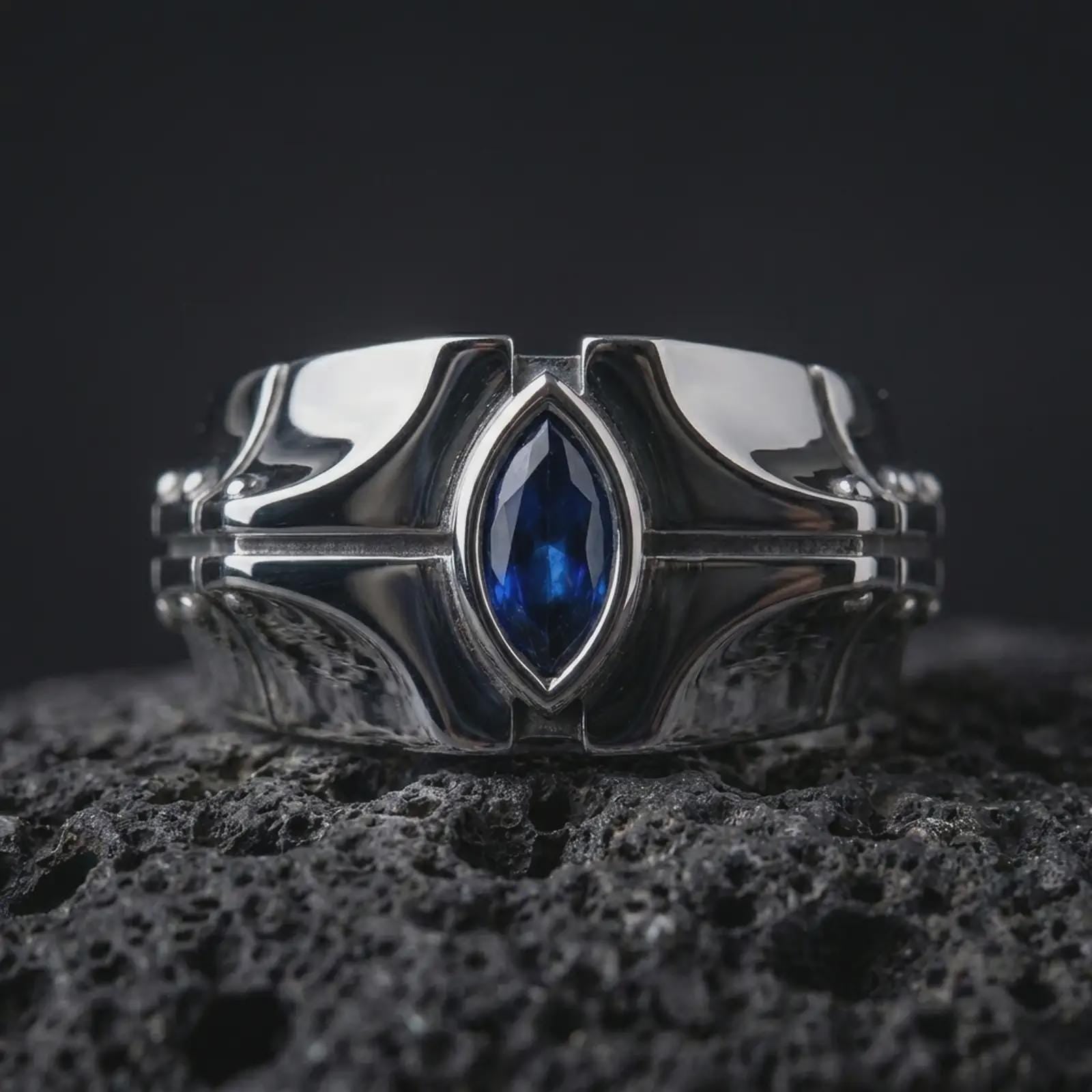 A sterling silver ring with a polished silver finish and marquise blue stone displayed on textured volcanic rock in a premium macro shot.