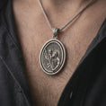 Load image into Gallery viewer, Oxidized Saint Christopher spinning pendant necklace worn on the chest, close-up lifestyle jewelry photo showing the Catholic traveler saint medal on a spiga chain with dark clothing.
