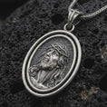 Load image into Gallery viewer, Oxidized spinning Jesus Christ pendant necklace on textured volcanic rock, close-up studio shot highlighting the crown of thorns portrait, oval frame, and antique silver contrast.
