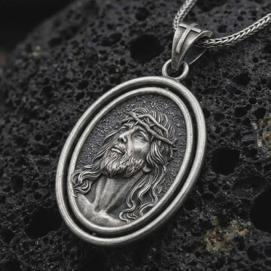 Oxidized spinning Jesus Christ pendant necklace on textured volcanic rock, close-up studio shot highlighting the crown of thorns portrait, oval frame, and antique silver contrast.