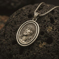 Load image into Gallery viewer, Bronze spinning Jesus Christ pendant necklace on textured volcanic rock, close-up studio shot highlighting the crown of thorns portrait, oval frame, and antique silver contrast.

