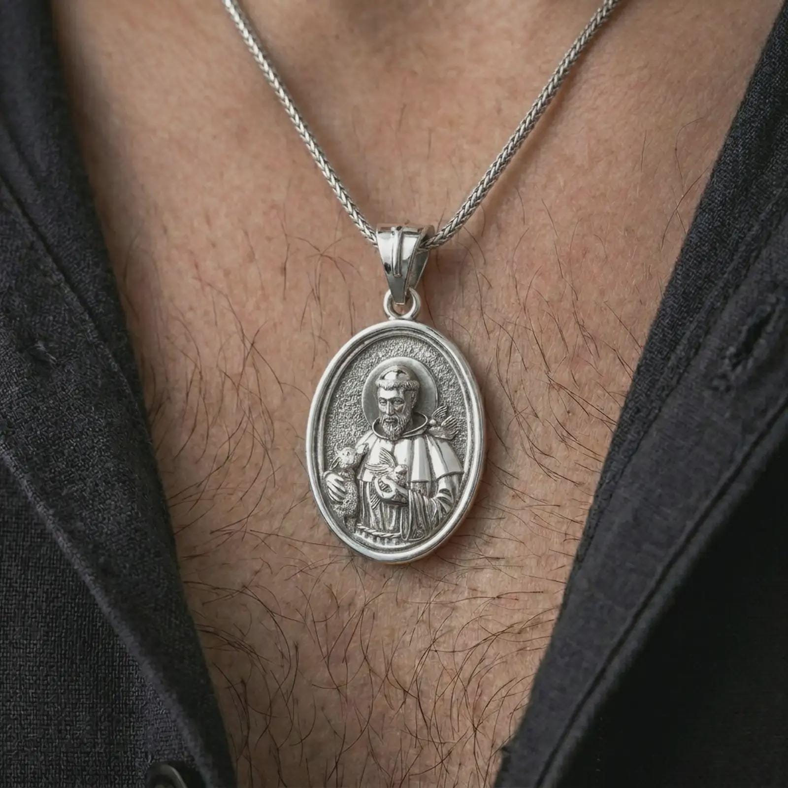 Polished silver Saint Francis pendant necklace worn on the chest, masculine lifestyle shot highlighting the saint relief, lamb, bird detail, and bright silver finish.