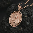 Load image into Gallery viewer, Rose gold plated Saint Francis pendant necklace on textured volcanic rock, detailed macro product shot with soft warm reflections and devotional Saint Francis design.
