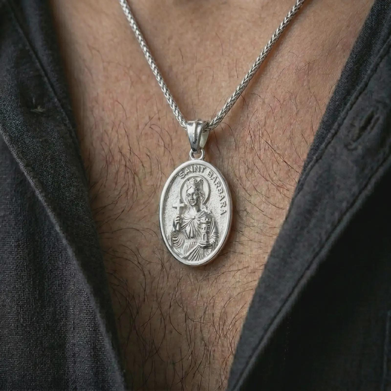 Polished silver Saint Barbara pendant necklace worn on the chest, masculine lifestyle shot highlighting the crowned saint relief, cross, tower detail, and bright silver finish.