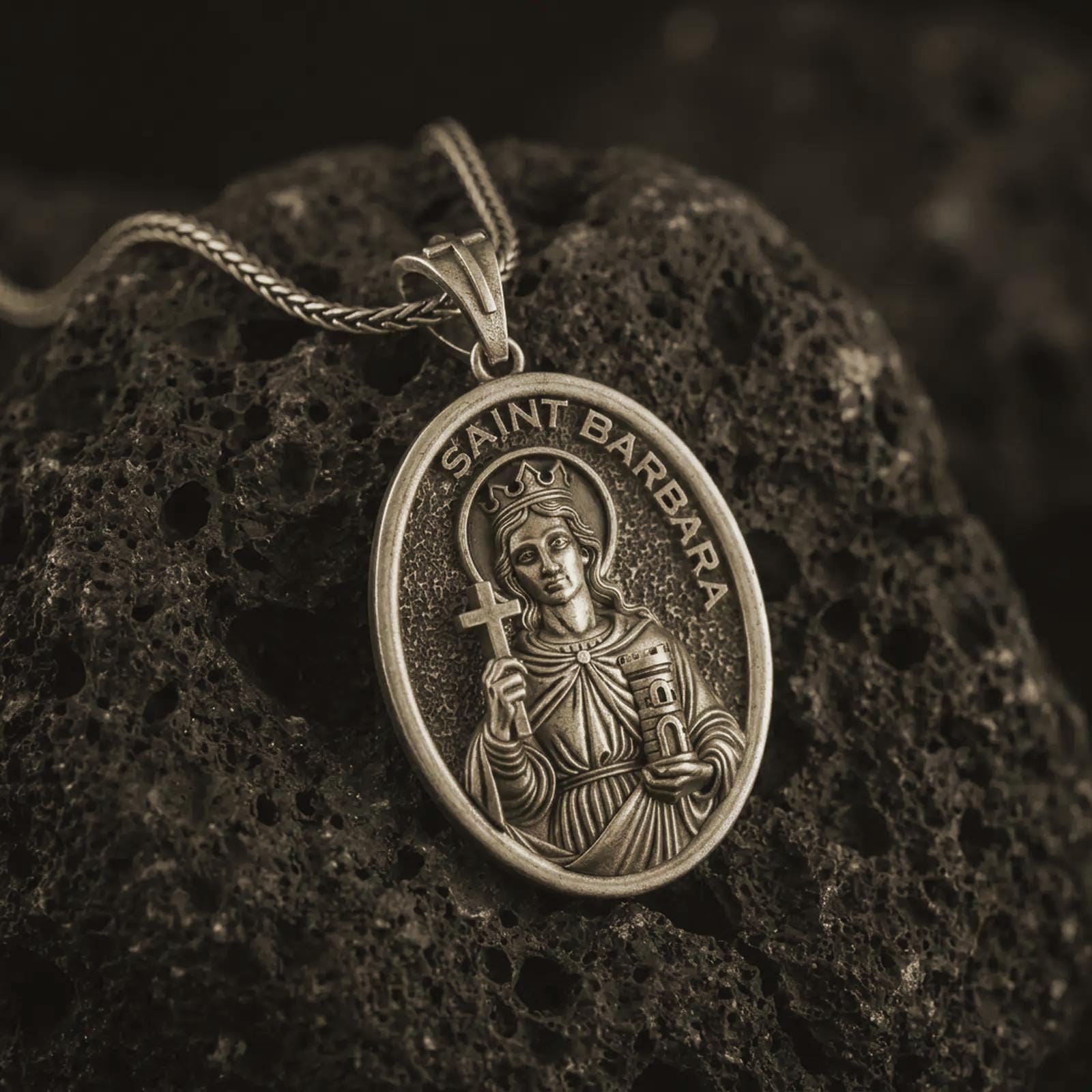 Bronze Saint Barbara pendant necklace on textured volcanic rock, close-up studio shot highlighting the crowned saint relief, cross, tower detail, and antique silver contrast.