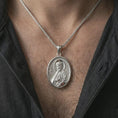 Load image into Gallery viewer, Polished silver Saint James the Apostle pendant necklace worn on the chest, masculine lifestyle shot highlighting the apostle relief, halo, book detail, and bright silver finish.
