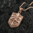 Load image into Gallery viewer, Rose gold plated knight shield pendant necklace on textured volcanic rock, detailed macro product shot with soft warm reflections and medieval knight symbolism.
