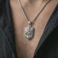 Load image into Gallery viewer, Polished silver knight shield pendant necklace worn on the chest, masculine lifestyle shot highlighting the armored knight relief, sword detail, and bright silver finish.
