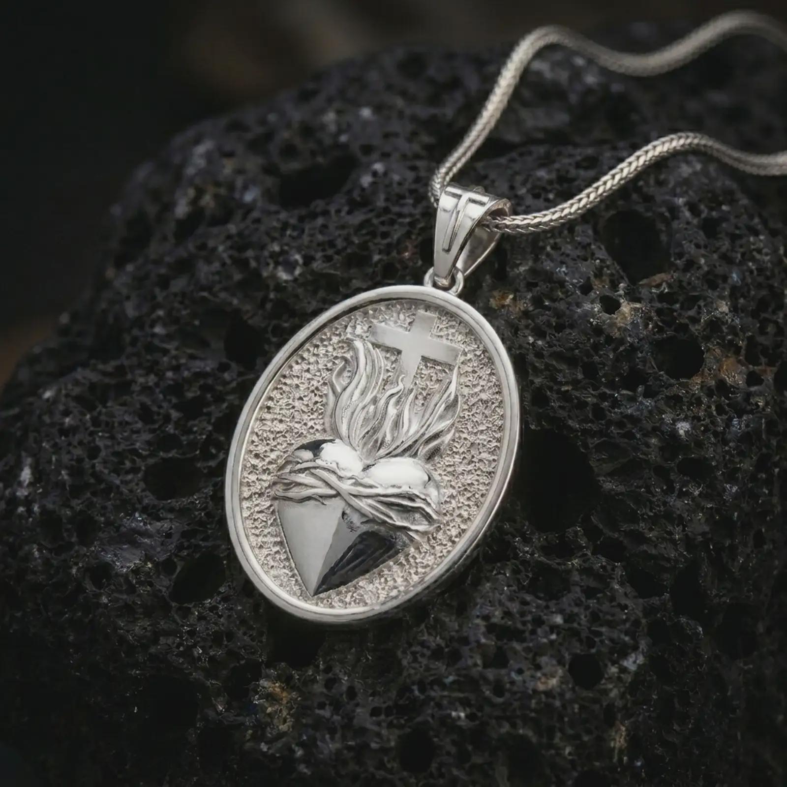 Polished silver Sacred Heart pendant necklace on textured volcanic rock, centered macro jewelry photo with detailed Catholic relief and bright silver highlights.