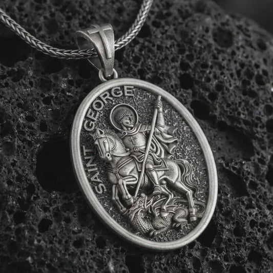 Oxidized Saint George pendant necklace on textured volcanic rock, close-up studio shot highlighting the mounted saint, spear, dragon detail, and antique silver contrast.