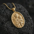 Load image into Gallery viewer, Gold plated Saint Joseph and Jesus pendant necklace on textured volcanic rock, premium close-up studio composition emphasizing Saint Joseph, child Jesus, lily, and sacred heart symbolism.
