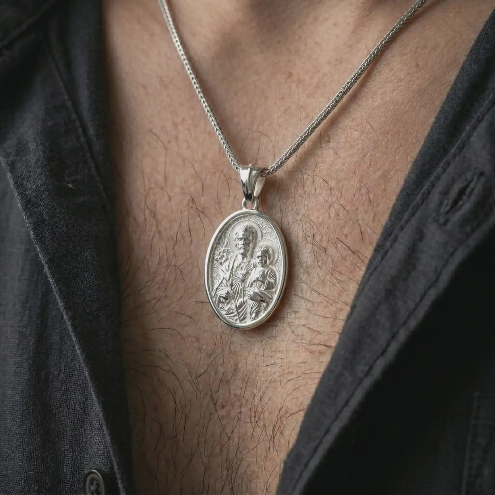 Polished silver Saint Joseph and Jesus pendant necklace worn on the chest, masculine lifestyle shot highlighting the father and child relief, lily detail, sacred heart, and bright silver finish.