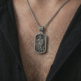 Load image into Gallery viewer, Oxidized Saint Roch dog tag pendant necklace worn on the chest, close-up lifestyle jewelry photo showing the Catholic patron medallion on a spiga chain with dark clothing.
