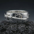 Load image into Gallery viewer, Polished silver Bushido sword band ring on textured volcanic rock, centered macro jewelry photo with detailed samurai-inspired sword relief and bright silver highlights.
