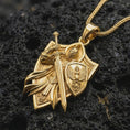 Load image into Gallery viewer, Gold plated crusader knight pendant on black volcanic rock, sharp focus on sword and shield engraving.
