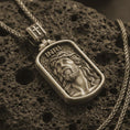 Load image into Gallery viewer, Bronze INRI Jesus pendant necklace on textured volcanic rock, close-up studio shot highlighting the crown of thorns portrait, raised relief, and antique silver contrast.
