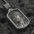 Load image into Gallery viewer, Oxidized INRI Jesus pendant necklace on textured volcanic rock, close-up studio shot highlighting the crown of thorns portrait, raised relief, and antique silver contrast.
