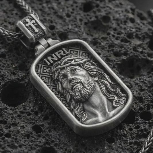 Oxidized INRI Jesus pendant necklace on textured volcanic rock, close-up studio shot highlighting the crown of thorns portrait, raised relief, and antique silver contrast.