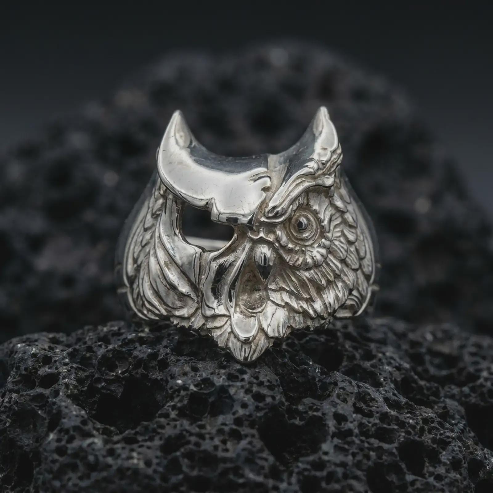 Polished sterling silver owl ring shot on textured volcanic rock in a centered macro composition with crisp detail.