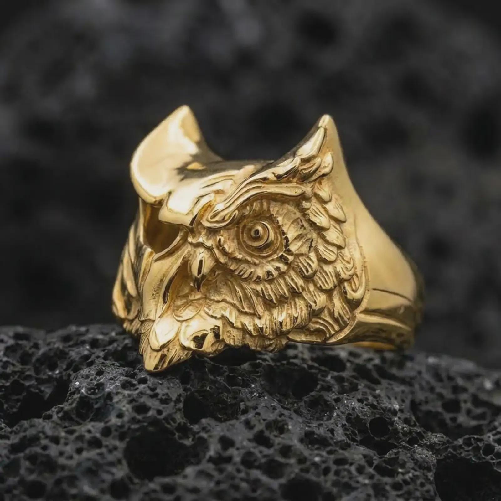 Gold plated owl ring captured on porous volcanic rock in the same close-up studio composition, highlighting the engraved feathers.