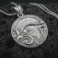Load image into Gallery viewer, A polished silver Eye of Horus pendant is displayed on black volcanic rock in a premium macro studio close-up with detailed ancient-style engraving.
