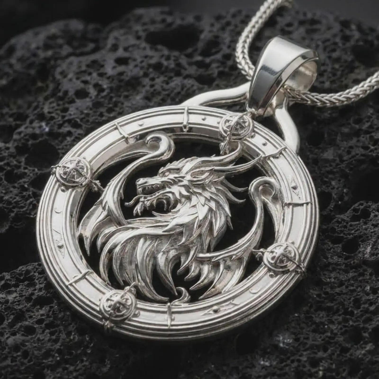 A polished silver dragon pendant is displayed on black volcanic rock in a premium macro studio close-up with sharp fantasy-inspired texture.
