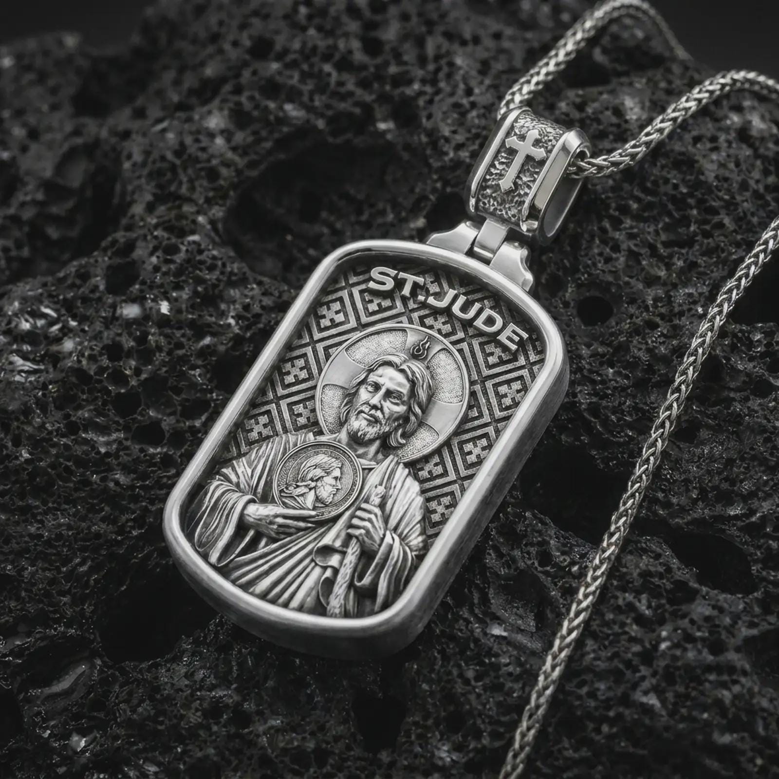 Polished silver Saint Jude dog tag pendant necklace on textured volcanic rock, centered macro jewelry photo with detailed Christian medal engraving and bright silver highlights.