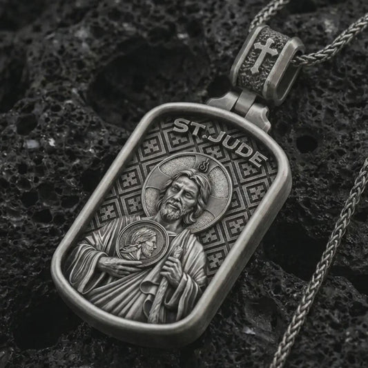 Oxidized Saint Jude dog tag pendant necklace on textured volcanic rock, close-up studio shot highlighting the saint relief, halo, medallion detail, and antique silver contrast.