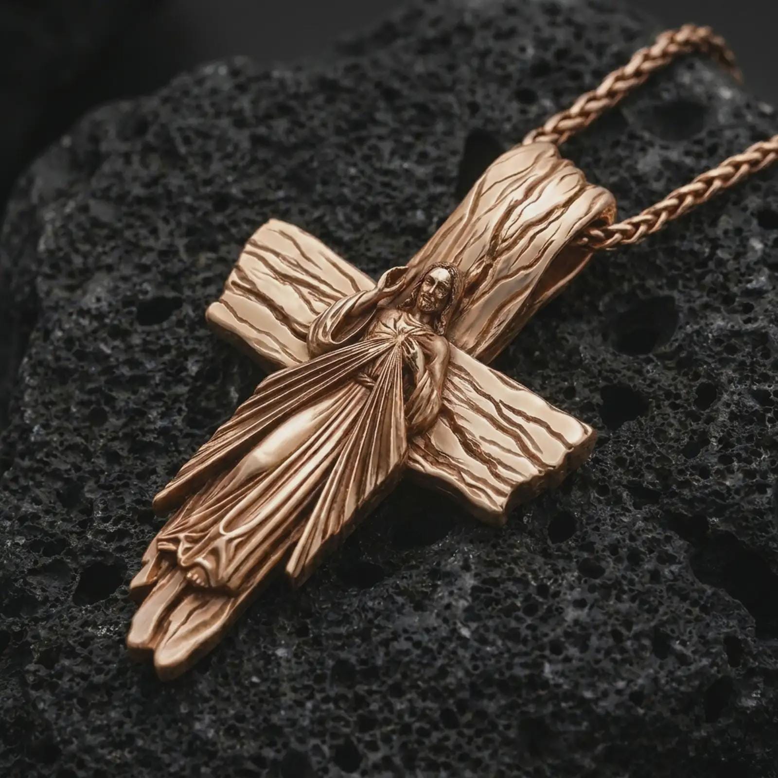 Rose gold plated Jesus cross pendant necklace on textured volcanic rock, detailed macro product shot with soft warm reflections and devotional Christ cross symbolism.