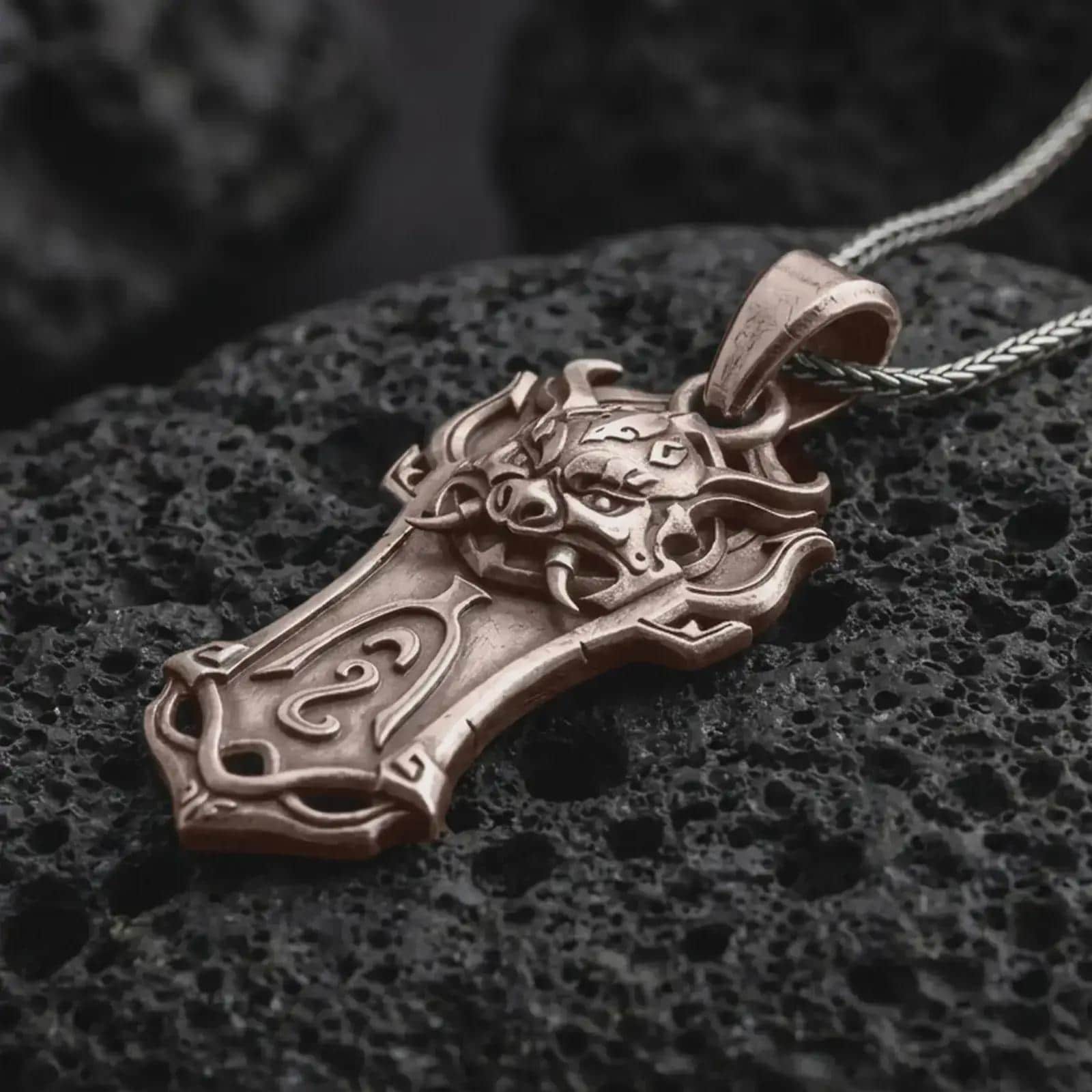 A Bronze Taurus bull pendant rests on dark volcanic rock in a macro studio close-up, showing a horned animal head over a shield-inspired frame.