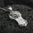 Load image into Gallery viewer, A polished silver Taurus bull pendant is displayed on black volcanic rock in a premium macro studio close-up with detailed horns and strong sculpted texture.
