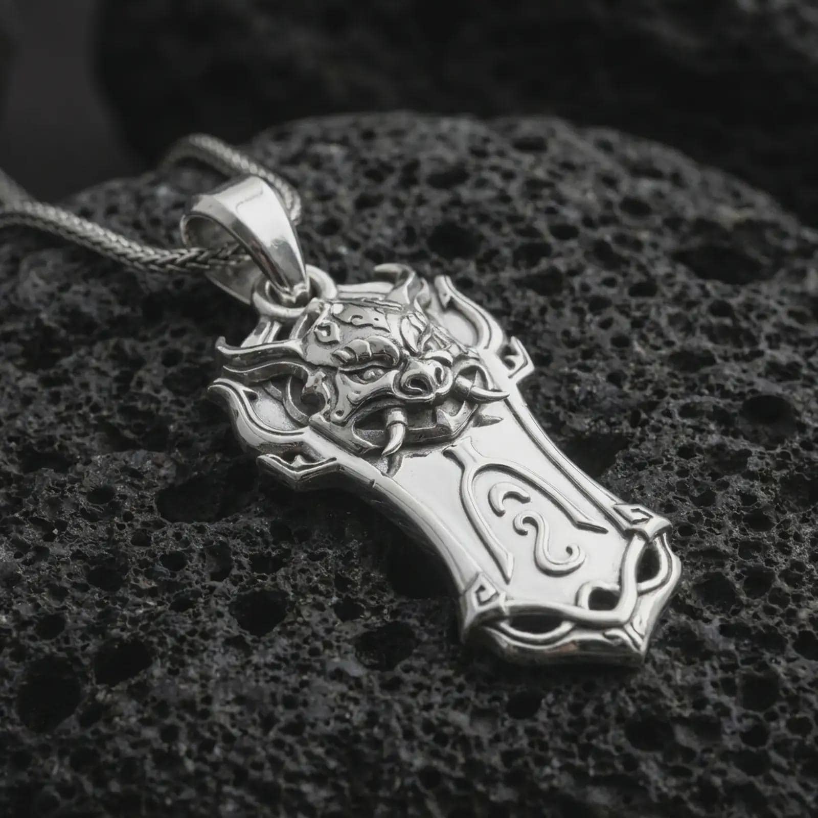 A polished silver Taurus bull pendant is displayed on black volcanic rock in a premium macro studio close-up with detailed horns and strong sculpted texture.
