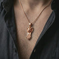 Load image into Gallery viewer, A rose gold plated Taurus bull pendant is worn on the neck in a close-up lifestyle composition, highlighting its shield-like frame and bold bull design.
