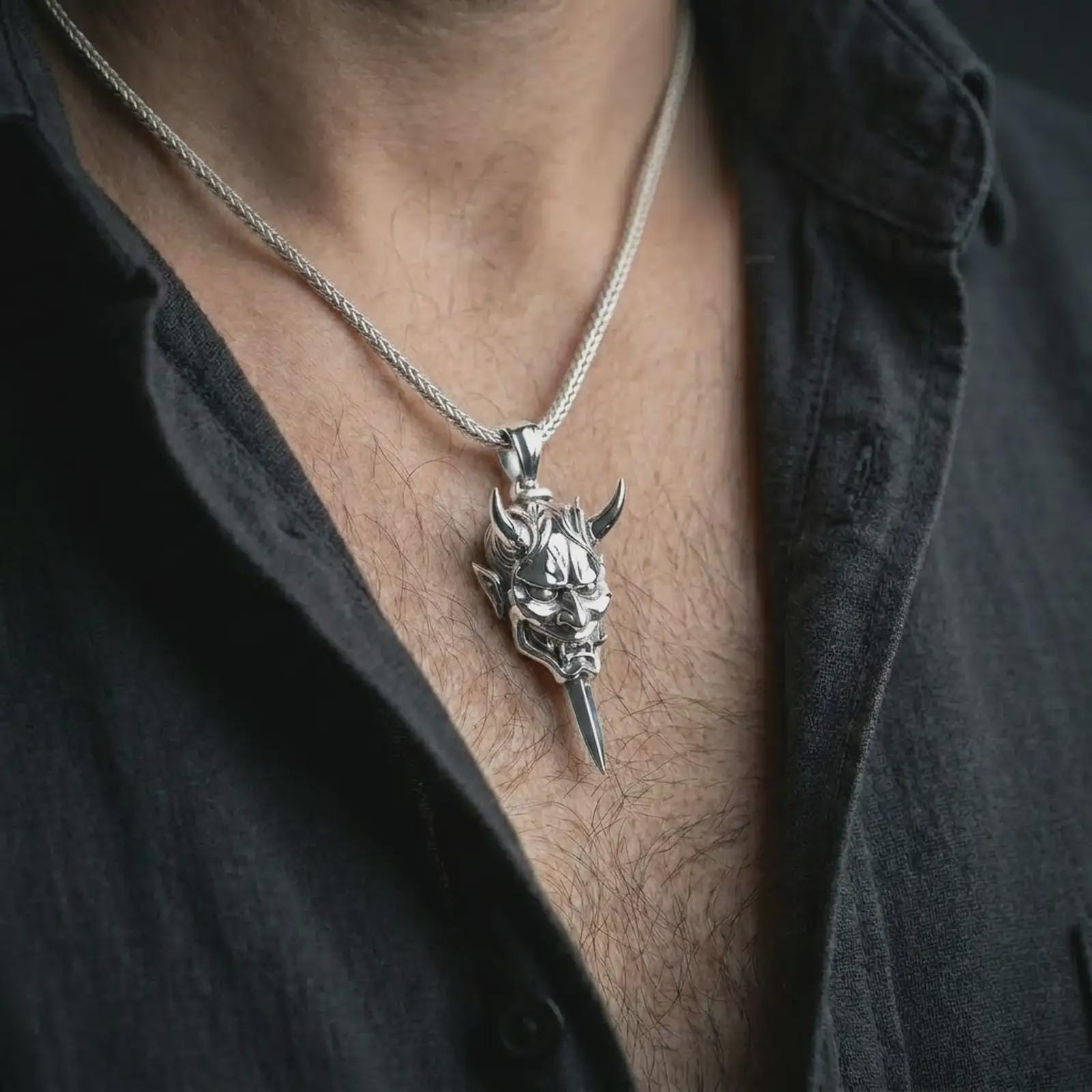 A polished silver oni mask pendant is worn on the neck in a premium close-up lifestyle image, showing the horned demon motif clearly.