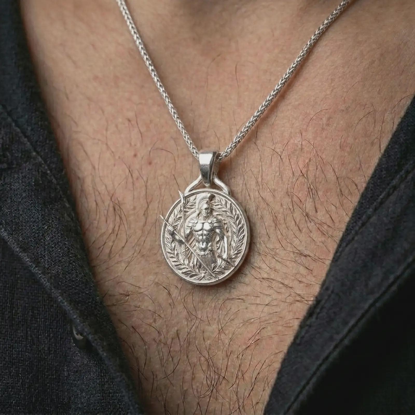 A polished silver Spartan warrior pendant is worn on the neck in a premium close-up lifestyle image, showing the Greek soldier motif clearly.