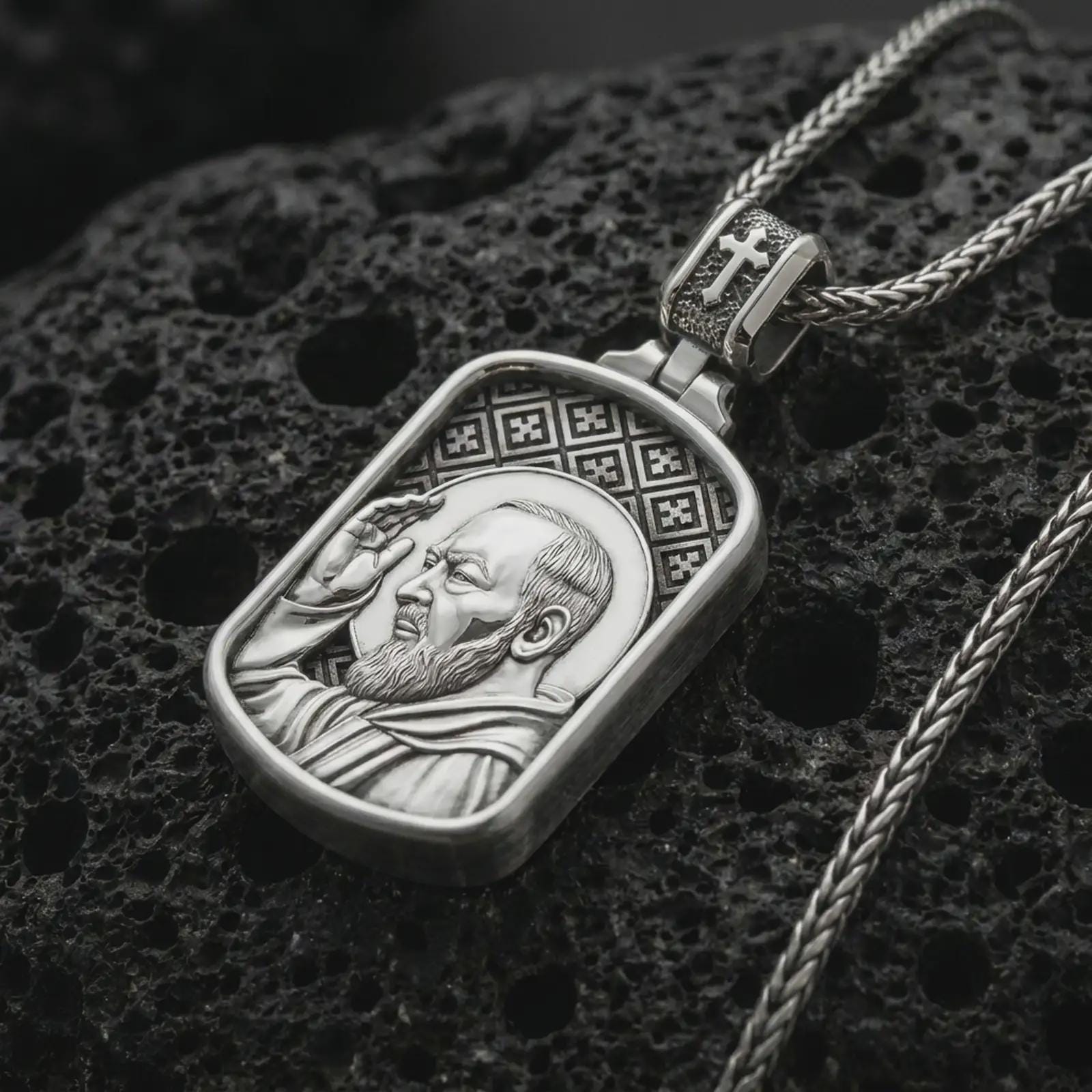 Polished silver Saint Padre Pio dog tag pendant necklace on textured volcanic rock, centered macro jewelry photo with detailed Christian relief and bright silver highlights.
