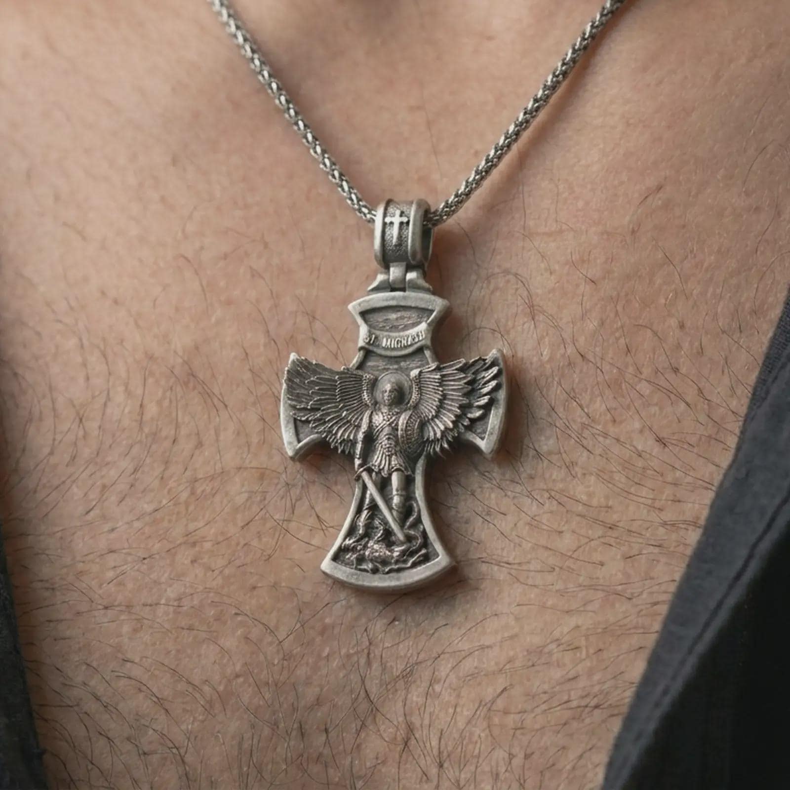 Oxidized Saint Michael cross pendant necklace worn on the chest, close-up lifestyle jewelry photo showing the religious archangel pendant on a spiga chain with dark clothing.