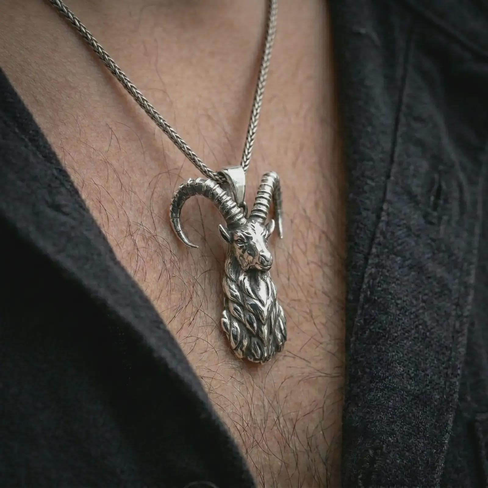 Polished silver ram horn pendant necklace worn on the chest, masculine lifestyle shot highlighting the sculpted ram head, curved horns, and bright silver finish.