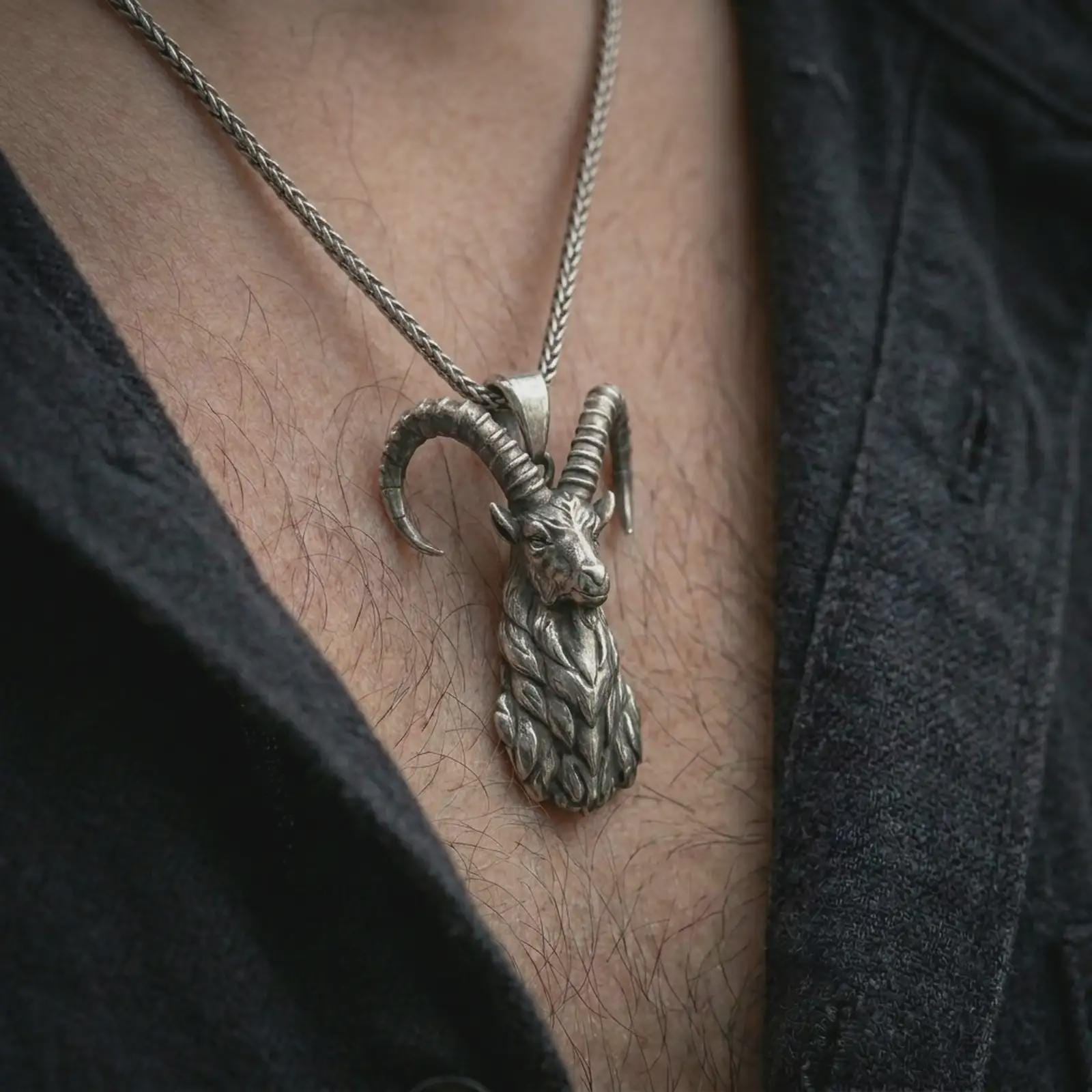 Oxidized ram horn pendant necklace worn on the chest, close-up lifestyle jewelry photo showing the Aries goat talisman on a spiga chain with dark clothing.