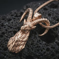 Load image into Gallery viewer, Rose gold plated ram horn pendant necklace on textured volcanic rock, detailed macro product shot with soft warm reflections and bold mythic animal symbolism.
