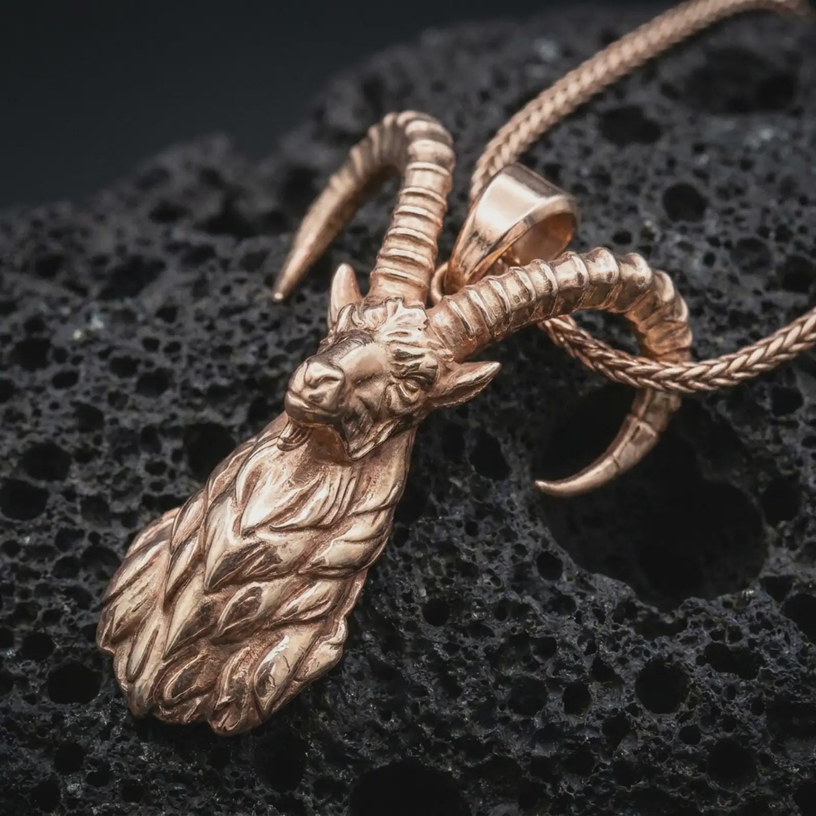 Rose gold plated ram horn pendant necklace on textured volcanic rock, detailed macro product shot with soft warm reflections and bold mythic animal symbolism.