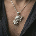 Load image into Gallery viewer, Polished silver chameleon pendant necklace worn on the chest, masculine lifestyle shot highlighting the detailed lizard form, curled tail, and bright silver finish.
