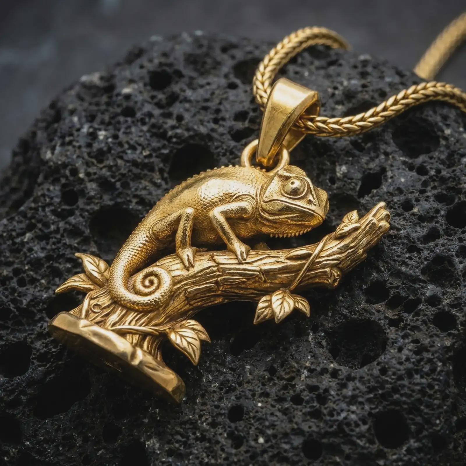 Gold plated chameleon pendant necklace on textured volcanic rock, premium close-up studio composition emphasizing the climbing lizard, curled tail, and nature-inspired branch design.