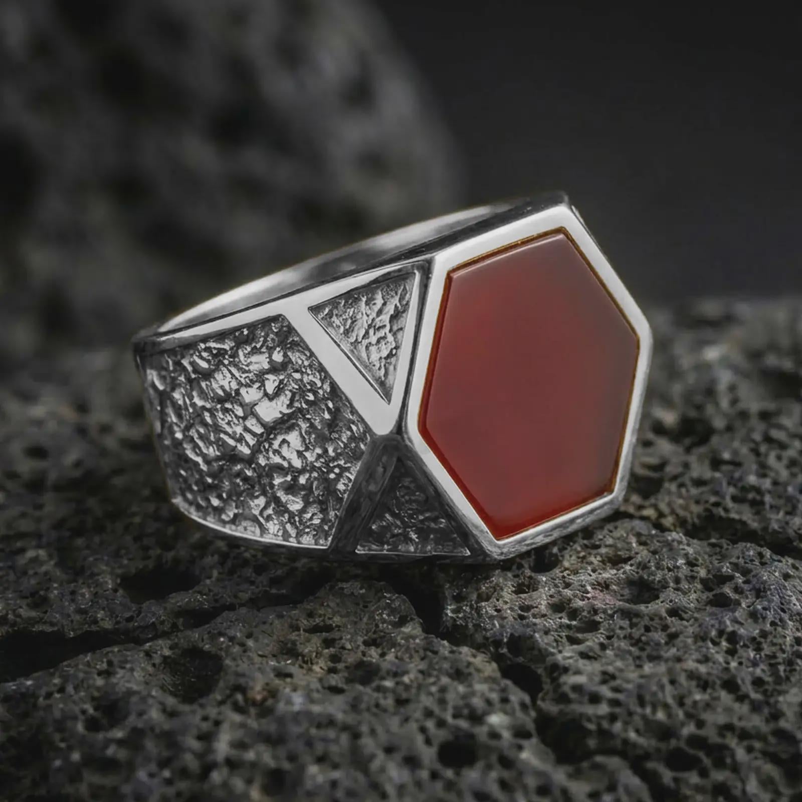 A red onyx signet ring in a polished silver finish resting on porous volcanic rock in a premium macro studio shot.