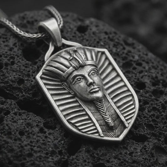 Oxidized pharaoh shield pendant necklace on textured volcanic rock, close-up studio shot highlighting the Egyptian king portrait, royal headdress, shield frame, and antique silver contrast.