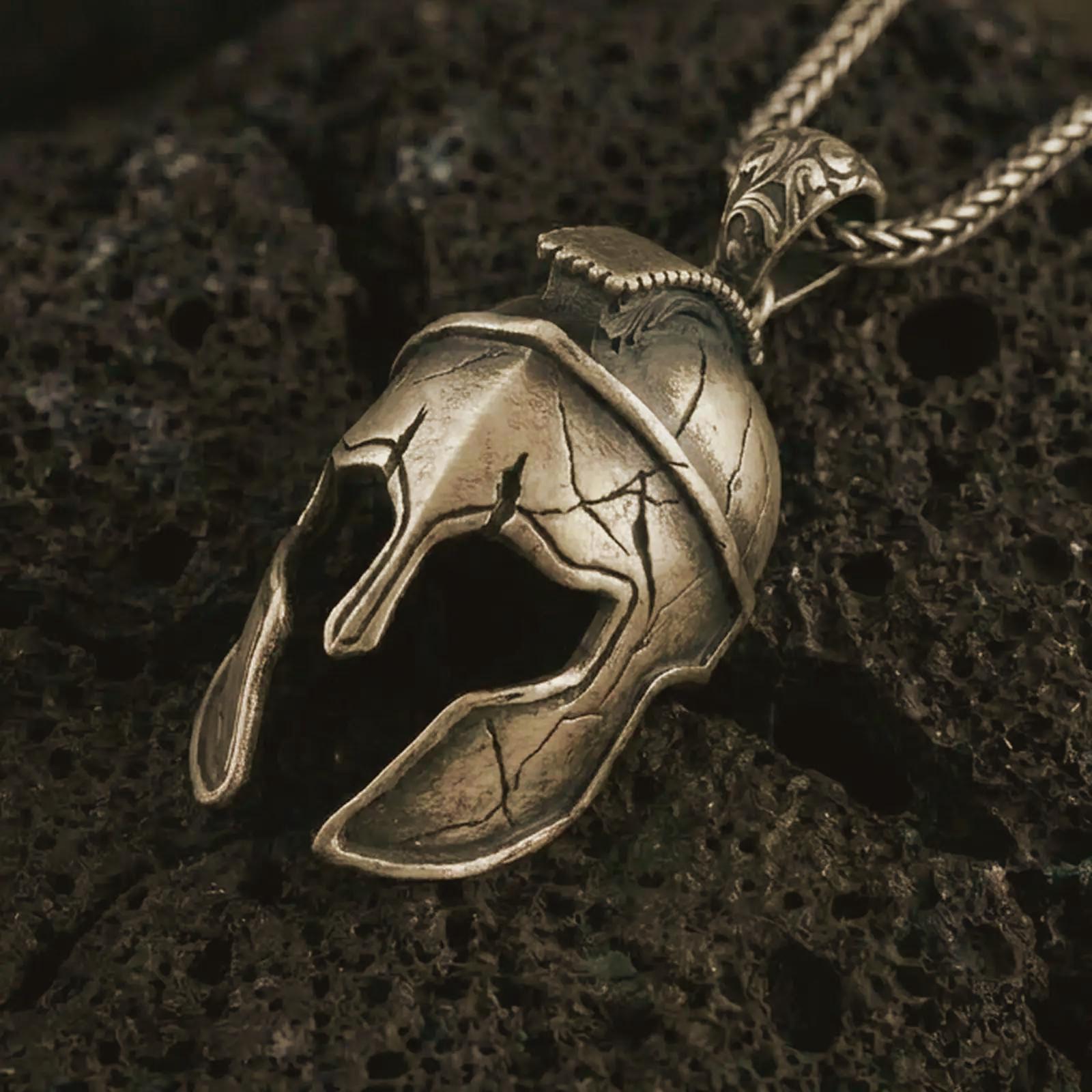 Bronze Spartan helmet pendant necklace on textured volcanic rock, close-up studio shot highlighting the cracked warrior helmet, open face guard, battle-worn texture, and antique silver contrast.