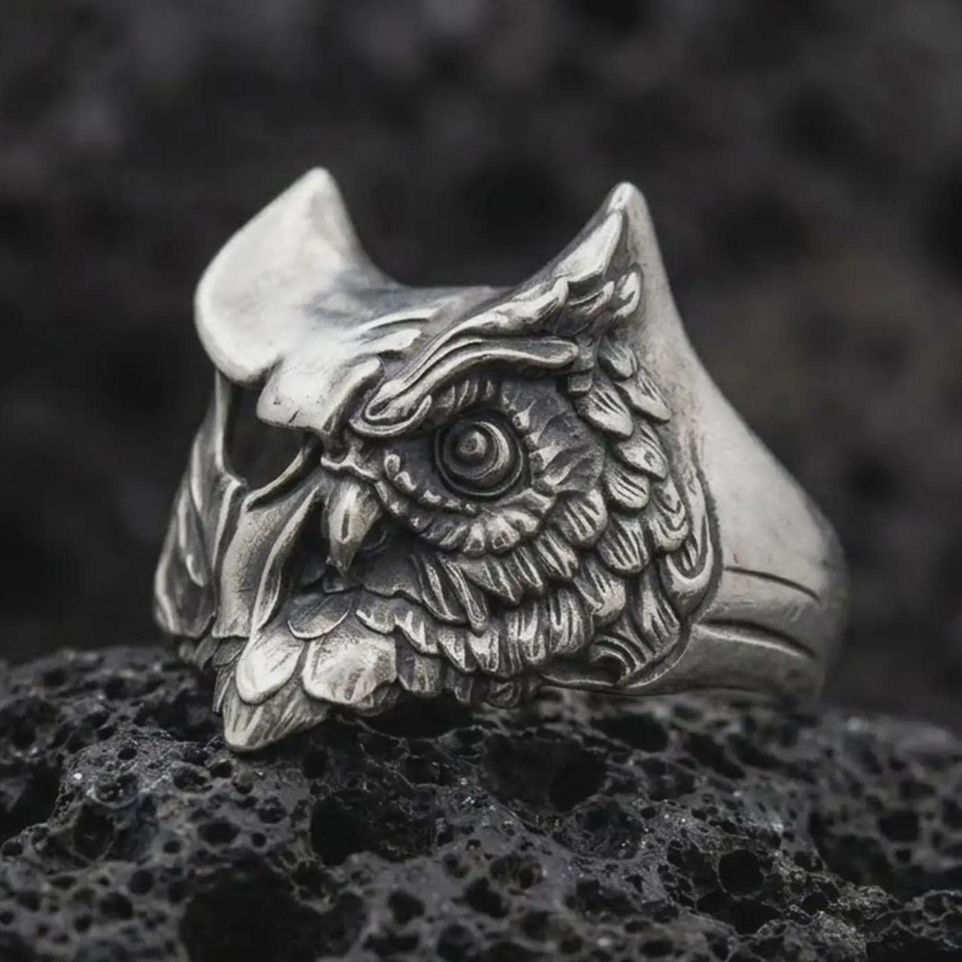 Oxidized sterling silver owl ring photographed close-up on black volcanic rock with a premium studio feel.
