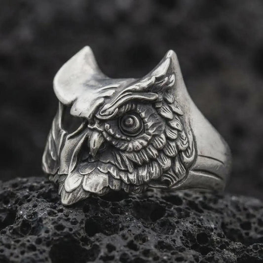 Oxidized sterling silver owl ring photographed close-up on black volcanic rock with a premium studio feel.