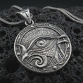 Load image into Gallery viewer, An oxidized Eye of Horus pendant rests on dark volcanic rock in a macro studio close-up, showing Egyptian-inspired details and a bold protection symbol.
